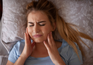 girl with jaw discomfort layng in bed holding her jaw 