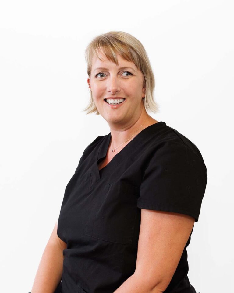 Headshot of Tanya sitting and wearing black scrubs against a plain white background.