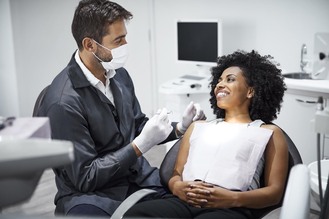 Doctor examining young woman on dentist's chair. Male is checking smiling patient in examination room. They are in clinic.