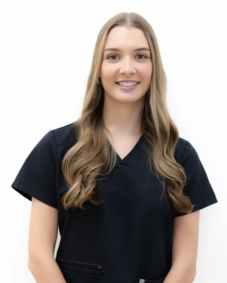 Arielle, dental hygienist, portrait against plain white background with long wavy light brown hair, wearing black short‑sleeved scrub top, facing forward with neutral expression.
